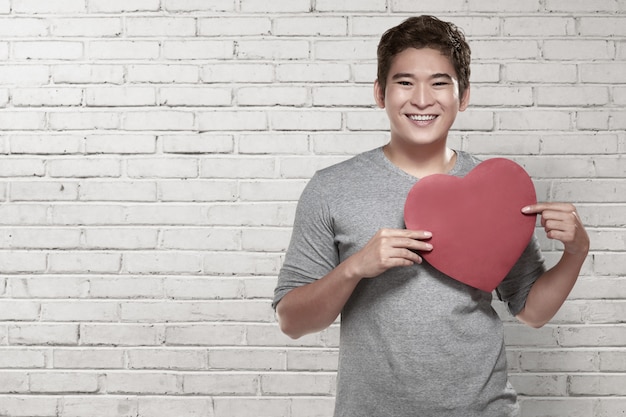 Uomo asiatico bello che tiene simbolo rosso del cuore