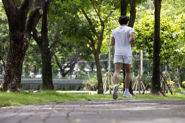 Uomo asiatico bello in camicia bianca che corre nel parco Concetto per uno stile di vita salutare nel parco