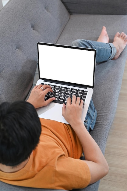 Uomo asiatico casual che riposa sul divano e naviga in Internet sul computer portatile