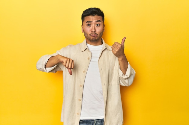 Uomo asiatico casuale con camicia aperta T-shirt bianca su studio giallo che mostra i pollici su e i pollici giù