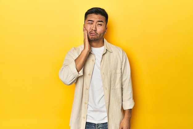 Uomo asiatico casuale con camicia aperta T-shirt bianca su studio giallo con un forte dolore ai denti dolore molare