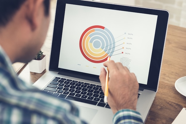 Uomo asiatico che analizza e che lavora con il diagramma finanziario di affari sul computer portatile a casa