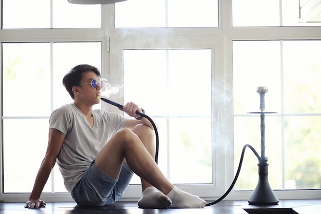 Uomo asiatico che fuma un narghilè alla finestra