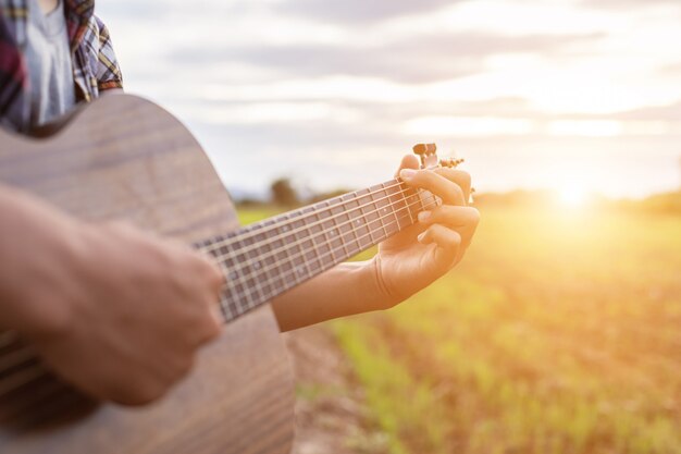 Uomo asiatico che gioca chitarra al giacimento verde del riso nel tempo di tramonto