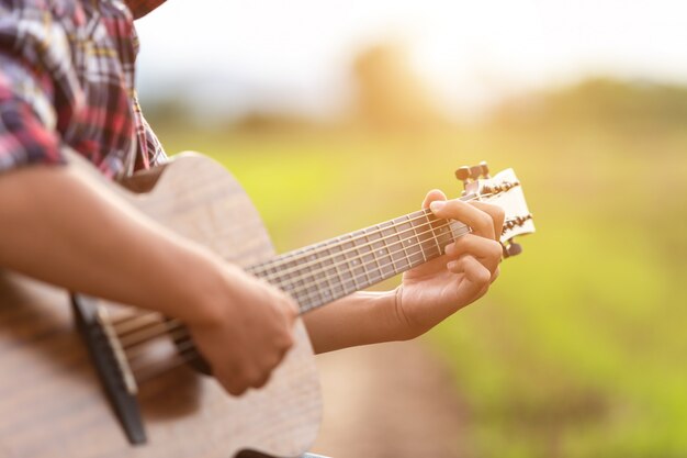 Uomo asiatico che gioca chitarra al giacimento verde del riso nel tempo di tramonto