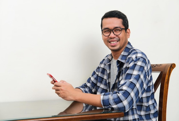 Uomo asiatico che guarda e sorride alla fotocamera mentre utilizza il telefono cellulare