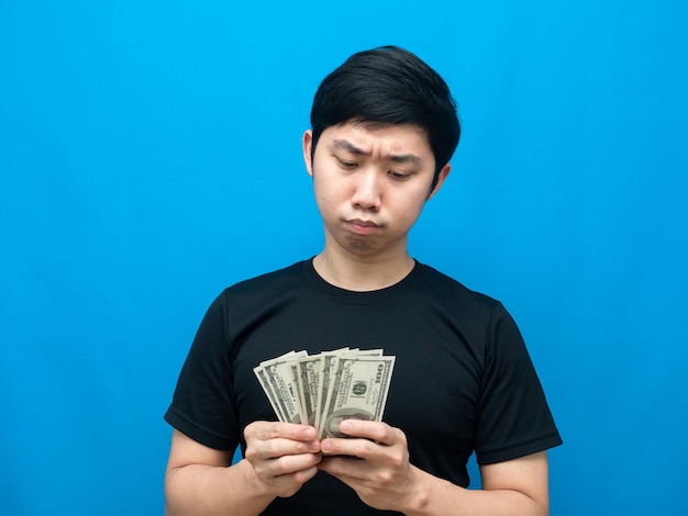 Uomo asiatico che guarda i soldi in mano e si sente dubbioso sullo sfondo blu