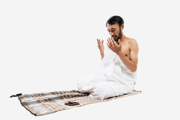 Uomo asiatico che indossa abiti ihram che pregano con un tappeto da preghiera