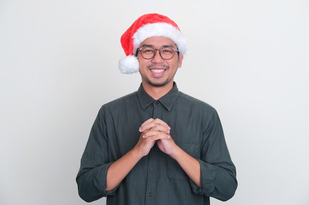 Uomo asiatico che indossa il cappello di Natale sorride alla macchina fotografica con la posa di preghiera della mano