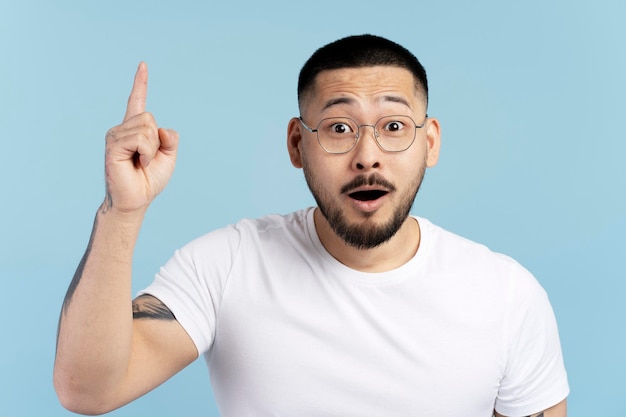 Uomo asiatico che indossa occhiali tenendo il dito alzato con un'idea creativa isolata su sfondo blu