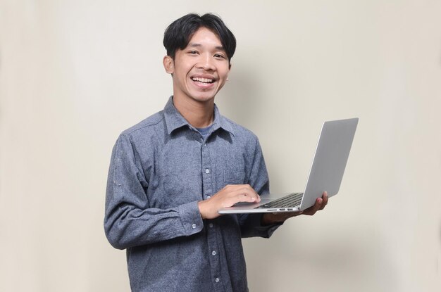 Uomo asiatico che indossa una camicia grigia che tiene il computer portatile su sfondo isolato