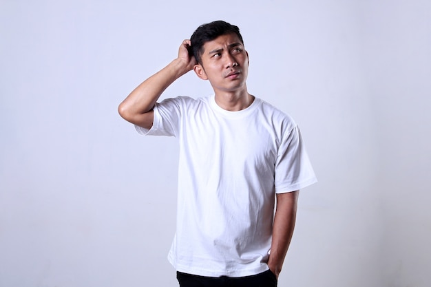 Uomo asiatico che indossa una maglietta bianca con espressione confusa isolato su uno sfondo bianco