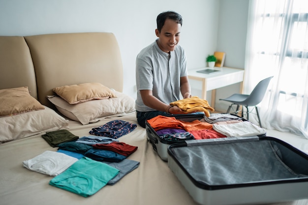 Uomo asiatico che mette i suoi vestiti nella valigia