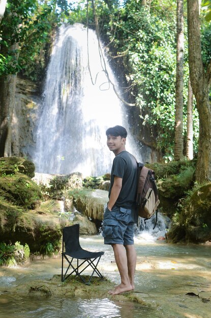 Uomo asiatico che porta zaino godendo della foresta davanti alla cascata