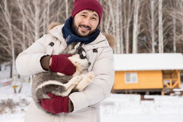Uomo asiatico che posa con il cucciolo in inverno