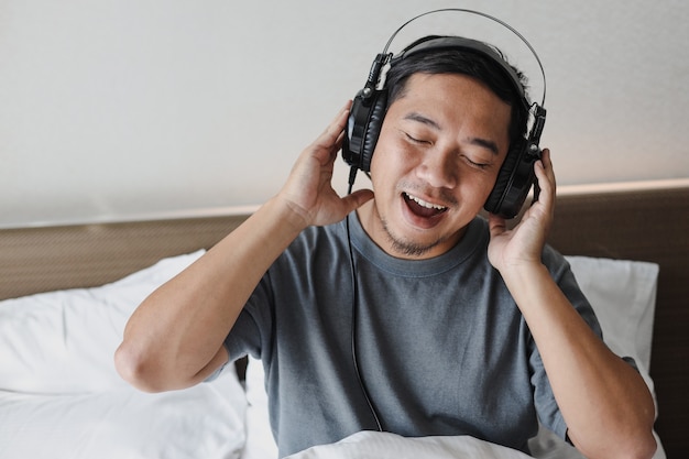 Uomo asiatico che si gode e ascolta una canzone dalle cuffie sul letto