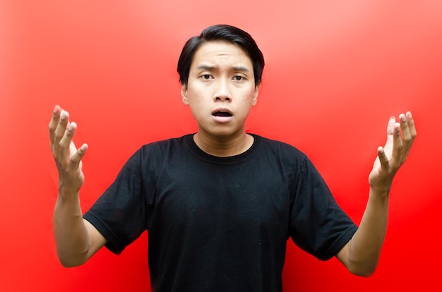 uomo asiatico che si interroga sul perché con espressione sconvolta, shock e confusa isolata su sfondo rosso.