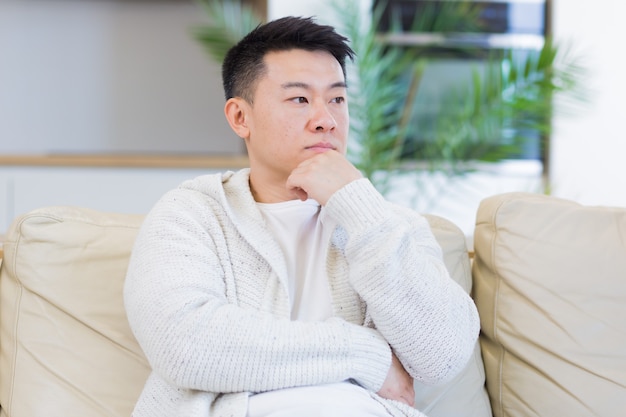 uomo asiatico che si tiene la testa con un forte mal di testa a casa in una stanza sul divano