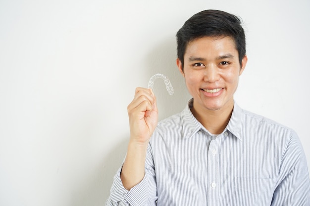 uomo asiatico che sorride con la mano che tiene fermo del dispositivo di allineamento dentale invisibile alla clinica dentale per il corso di trattamento dei bei denti