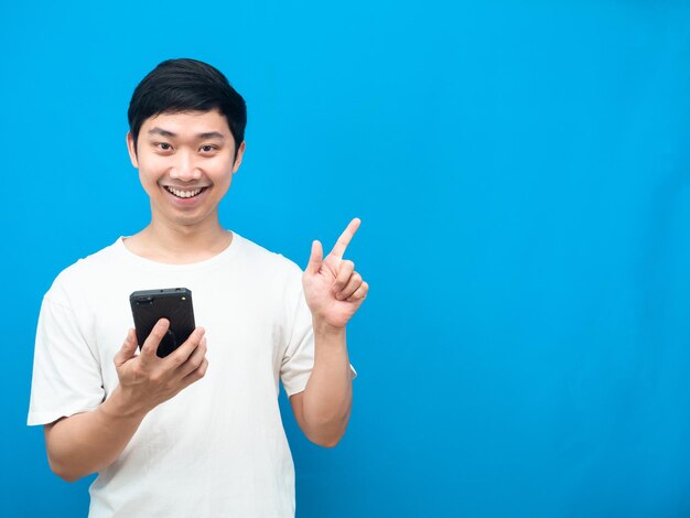 Uomo asiatico che tiene il telefono cellulare sorriso felice e punta il dito contro lo spazio della copia sfondo blu