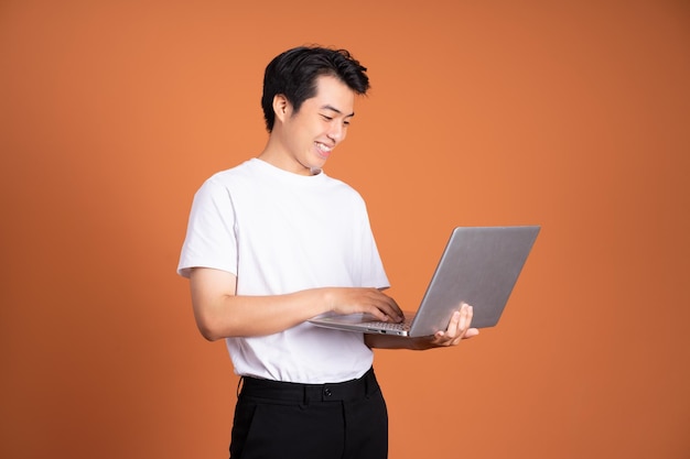 Uomo asiatico che tiene laptop isolato su sfondo arancione