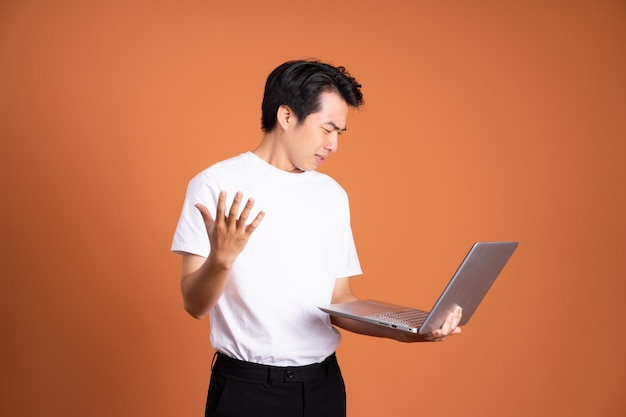 Uomo asiatico che tiene laptop isolato su sfondo arancione