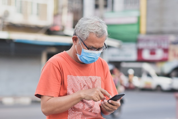 Uomo asiatico che tiene smart phone mobile Utilizzare la maschera per proteggere il virus corona PM2.5 camminando sulla strada nuova normale distanza sociale