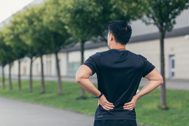 Uomo asiatico che trattiene il dolore alla schiena dopo la corsa e il fitness