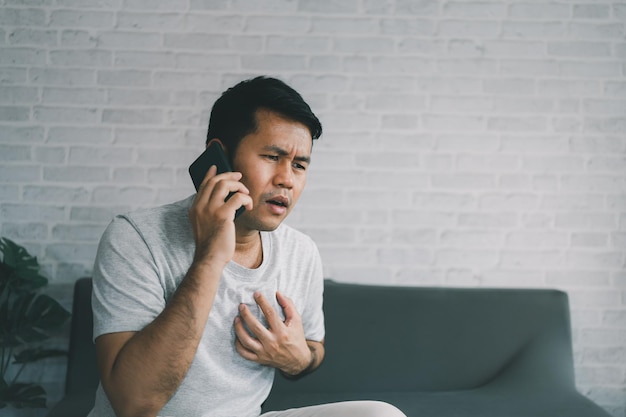 Uomo asiatico che utilizza lo smartphone per chiamare l'ospedale a causa di dolore toracico acuto sfondo grigio Concetto medico e sanitario