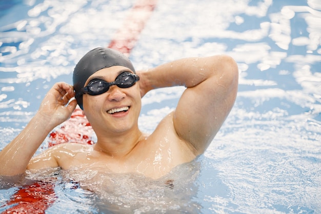 Uomo asiatico con cappello e occhiali che nuotano nella piscina interna