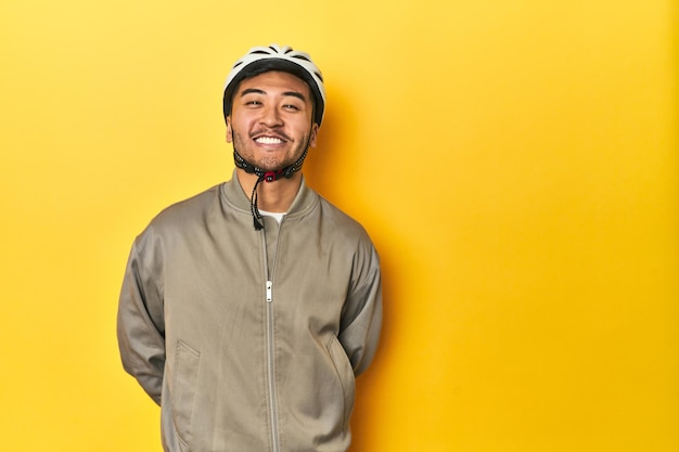 Uomo asiatico con casco da bicicletta e guanti sullo sfondo giallo dello studio felice sorridente e allegro