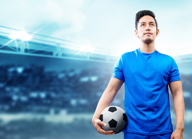 Uomo asiatico del giocatore di football americano in maglia blu che tiene la palla sul campo di football americano