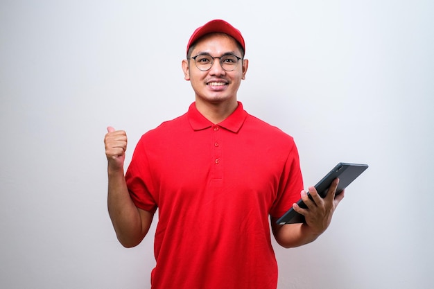 Uomo asiatico delle consegne che indossa il cappuccio che tiene lo smartphone su sfondo bianco molto felice che indica con la mano e il dito di lato