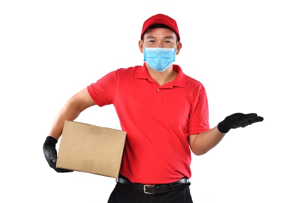 Uomo asiatico di consegna che indossa la maschera e guanti in uniforme rossa che consegna la cassetta dei pacchi isolata su bianco durante lo scoppio di COVID-19