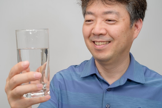 Uomo asiatico di mezza età che tiene un bicchiere d'acqua.