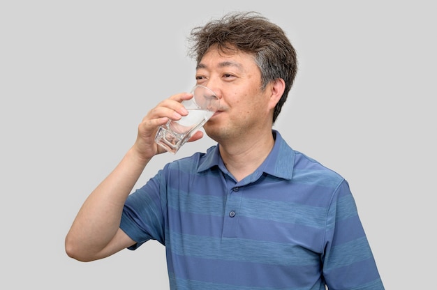 Uomo asiatico di mezza età che tiene un bicchiere d'acqua.