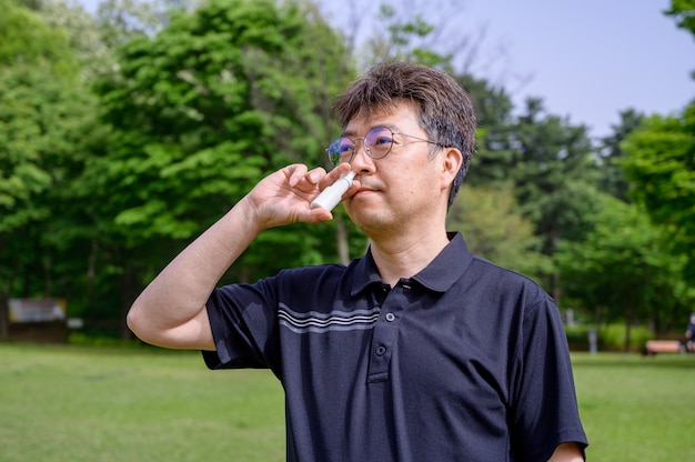 Uomo asiatico di mezza età che usa spray nasale all'aperto.