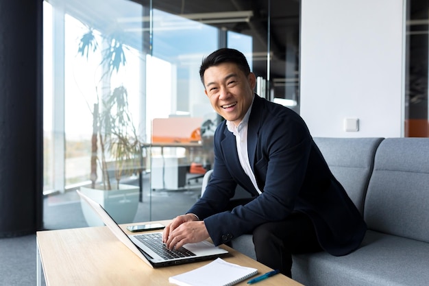 Uomo asiatico di successo e felice che lavora online in remoto sul laptop sorridente felice con il piano e l'attività