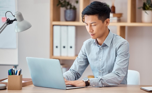 Uomo asiatico e laptop in ufficio per comunicazioni e-mail e affari su internet alla scrivania Digitazione al computer e lavoro in azienda per pubblicità di marketing digitale o lavoro seo durante la scrittura a Tokyo