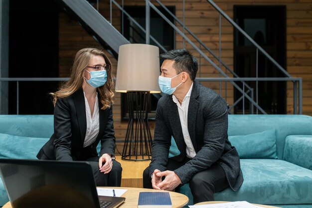 Uomo asiatico e una donna che indossano maschere mediche protettive seduti in ufficio al computer
