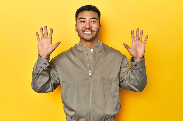 Uomo asiatico elegante in giacca grigia su uno studio giallo che mostra il numero dieci con le mani