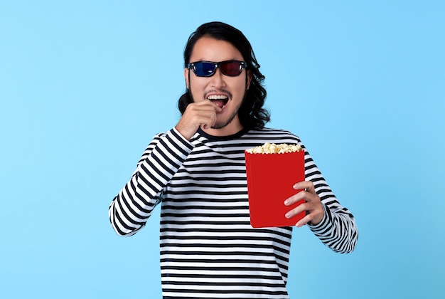 Uomo asiatico felice che indossa occhiali 3d e mangia popcorn mentre si guarda un film.