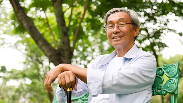 Uomo asiatico felice che si siede su un banco al parco.