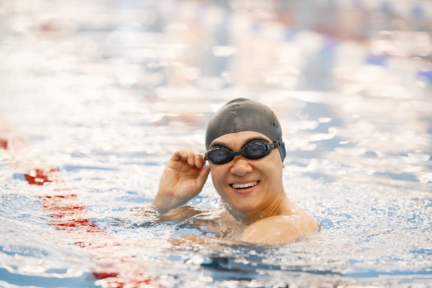 Uomo asiatico in cappello e occhiali che nuotano nella piscina interna