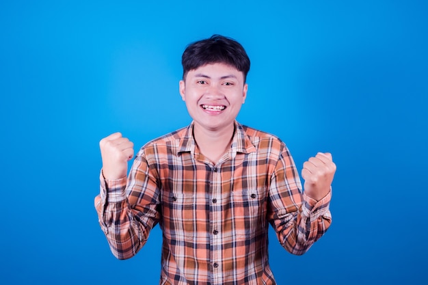 Uomo asiatico in Indossare una camicia a righe sorridente su sfondo blu, gioiosa che esprime celebrando la vittoria di buone notizie vincendo il successo