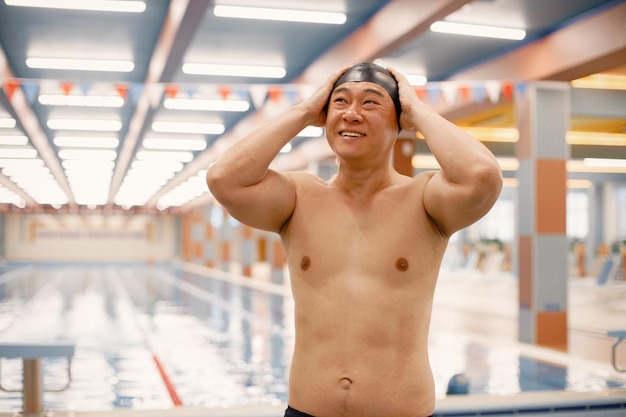 Uomo asiatico in piedi nella piscina interna e con indosso un cappello