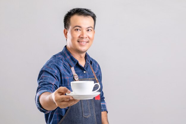 Uomo asiatico in uniforme da barista che tiene tazza di caffè