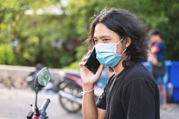 Uomo asiatico indossa maschera chirurgica mentre al telefono