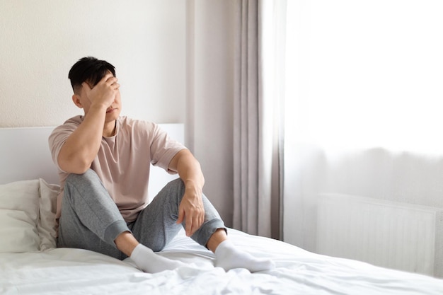 Uomo asiatico infelice seduto sul letto a casa copia spazio