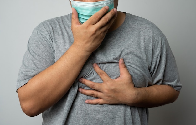 Uomo asiatico malato che indossa una maschera medica e tosse e si copre la bocca con la mano. Concetto di protezione coronavirus pandemico e malattie respiratorie